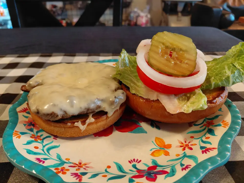 A grilled house burger topped with melted cheese, lettuce, tomato, onion and pickle, halved on a floral plate